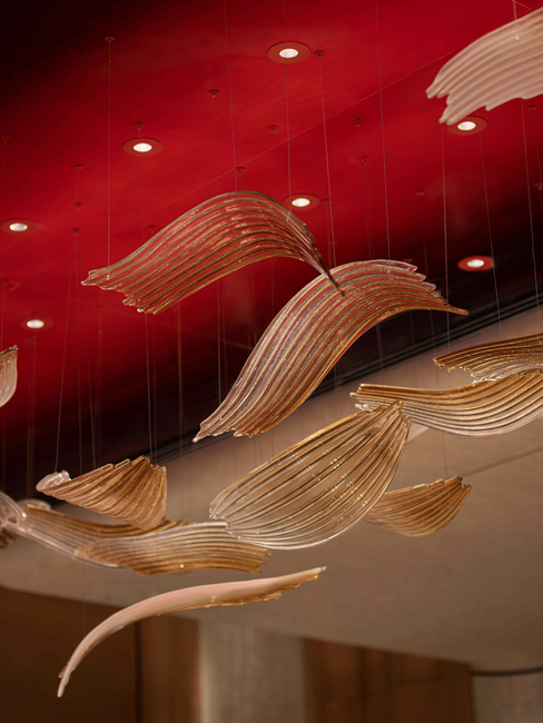 A high-gloss red lacquer ceiling serves as a vivid focal point, anchored by a sculptural crystal chandelier by Sans Souci.